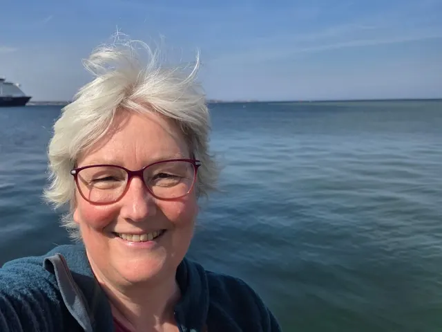 Selfie von Inken Kuhn auf dem Wasser, hinter ihr ein Kreuzfahrtschiff auf der Förde.