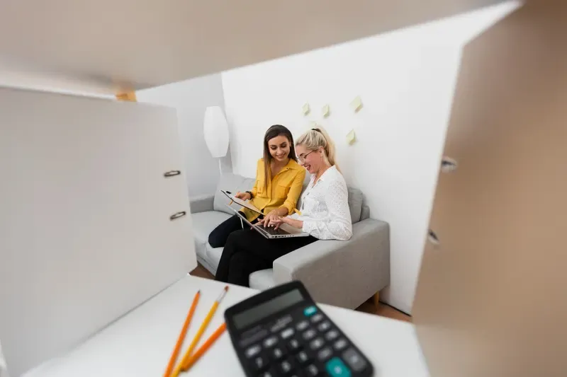 Zwei Frauen sitzen mit einem Laptop zusammen und sprechen miteinander.