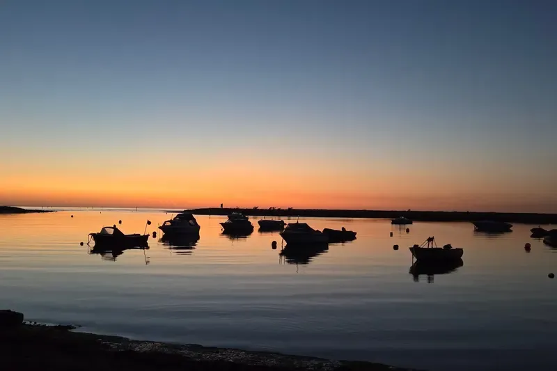 Boote liegen bei Sonnenuntergang im ruhigen Hafen, der Himmel leuchtet orange.