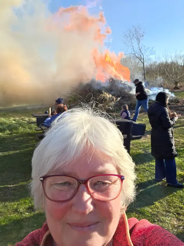 Selfie von Inken Kuhn bei einem Osterfeuer, im Hintergrund stehen Menschen auf der Wiese.